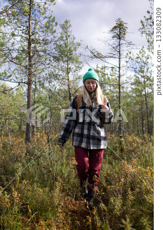 Woman hiker walking through marshy pine forest on her daily walk outdoors, enjoying pure nature. Woman hiker walking through marshy pine forest on her daily walk outdoors, enjoying pure nature. 133082309