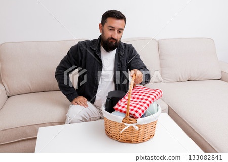 Caucasian male preparing picnic basket on living room sofa 133082841