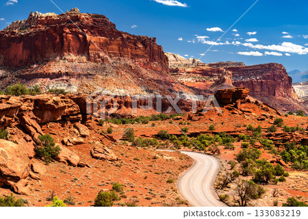 View from Panorama Point of the unpaved Goosenecks Road winding through Capitol Reef National Park. Massive red rock formations rise under a blue sky with clouds View from Panorama Point of the unpaved Goosenecks Road winding through Capitol Reef National Park. Massive red rock formations rise under a blue sky with clouds 133083219