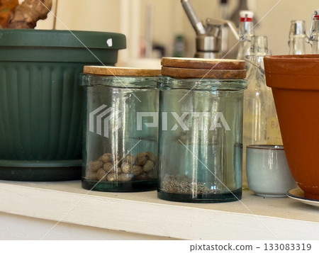 Glass jars with nuts and spices on white shelf. Cozy kitchen atmosphere, transparency, and simple everyday still life composition. 133083319