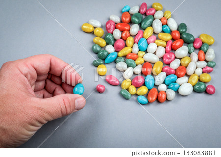 Hand picking colorful candy from pile on gray background symbolizing choice temptation and decision 133083881