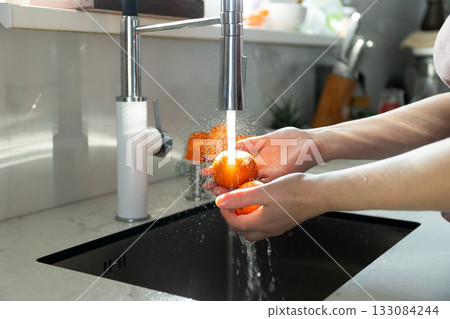 Washing Fresh Tangerines Under Running Water in a Kitchen Sink 133084244