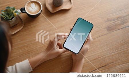 Woman reviewing finances on smartphone with coffee and plant nearby. Mobile banking, digital payments and financial planning in relaxed atmosphere Woman reviewing finances on smartphone with coffee and plant nearby. Mobile banking, digital payments and financial planning in relaxed atmosphere 133084631
