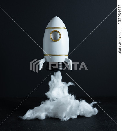 Toy rocket model on surface with white smoke clouds, evoking energy, motion, and futuristic space technology in miniature form, concept of adventure, science, and human exploration of space. 133084652