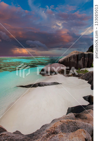 Crescent white sand and weathered granite at La Digue, Seychelles, face a teal lagoon. Pink and amber storm clouds move at dusk. Wide angle long exposure feel. Crescent white sand and weathered granite at La Digue, Seychelles, face a teal lagoon. Pink and amber storm clouds move at dusk. Wide angle long exposure feel. 133085013
