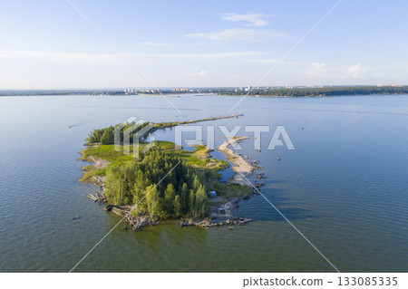 Aerial view of an island on a lake with trees, a sandbar and a forest on the horizon 133085335