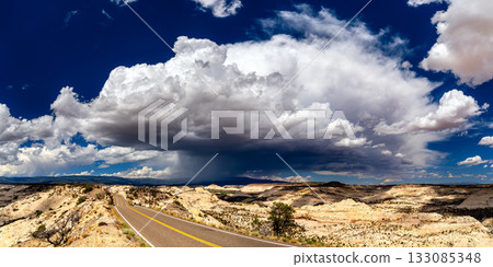 Utah State Route 12 winds over The Hogback in Grand Staircase-Escalante National Monument. A large, dramatic storm cloud with rain (virga) hangs over the vast slickrock landscape 133085348