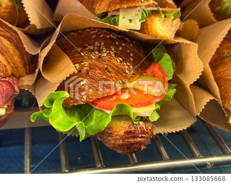 Croissant sandwiches with lettuce, tomato, and cheese in paper bags. Fresh breakfast, street food, and quick cafe meal concept. Close-up Croissant sandwiches with lettuce, tomato, and cheese in paper bags. Fresh breakfast, street food, and quick cafe meal concept. Close-up 133085668
