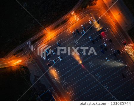 Aerial nighttime view of empty parking lot warm orange streetlights illuminate marked lanes and scattered cars, highlighting symmetry Aerial nighttime view of empty parking lot warm orange streetlights illuminate marked lanes and scattered cars, highlighting symmetry 133085744