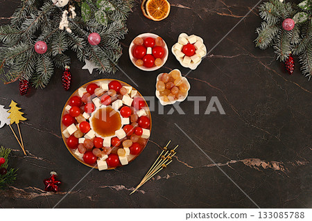 Christmas and New Year's dishes, traditional holiday salad with feta cheese, tomatoes, grapes, olives and honey with fir branches and decorations, dish decoration idea, menu template 133085788