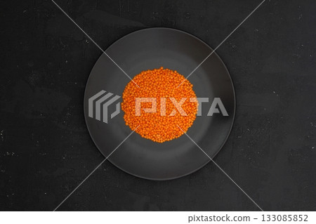 Red lentils in black plate on black stone table background. Top view, copy space. Flat lay. Red lentils in black plate on black stone table background. Top view, copy space. Flat lay. 133085852