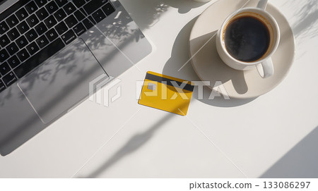 Yellow credit card on white desk with laptop and cup of black coffee in sunlight. Modern flat lay workspace concept for Cyber Monday online shopping and digital payment 133086297