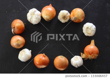 Onions and garlic over black background. Still-life of onions and falling garlic on black background Onions and garlic over black background. Still-life of onions and falling garlic on black background 133086437