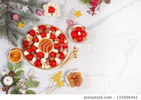 Festive New Year's salad with feta cheese, tomatoes, grapes, olives, and honey with fir branches and decorations, dish decoration idea, Christmas and New Year's dishes, menu template and banner 133086442