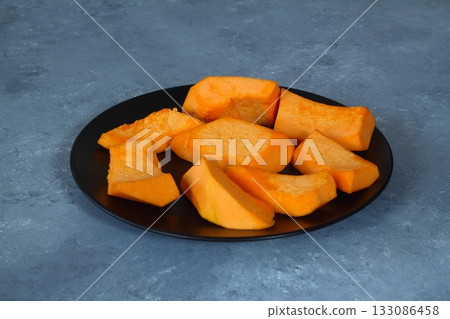 Slices of raw pumpkin with orange-yellow flesh in stainless steel bowl on a black background Slices of raw pumpkin with orange-yellow flesh in stainless steel bowl on a black background 133086458