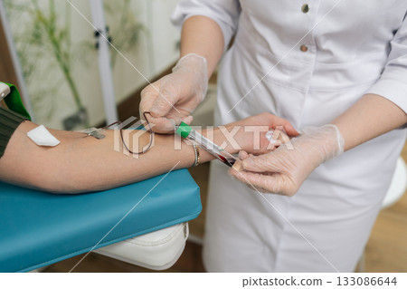 Healthcare professional female performing venipuncture on patient arm using vacuum tube system for blood collection, diagnostic testing and routine clinical care in medical clinic setting. 133086644