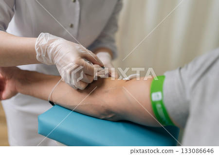 Medical professional in sterile gloves inserts needle into male patient arm vein to collect blood into tube for routine testing, diagnostic laboratory analysis, close-up. Concept of healthy lifestyle Medical professional in sterile gloves inserts needle into male patient arm vein to collect blood into tube for routine testing, diagnostic laboratory analysis, close-up. Concept of healthy lifestyle 133086646