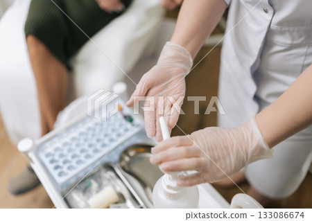Close-up top view of medical professional in protective gloves sanitizing hands with pump antiseptic on portable cart before procedure like blood sampling, with essential supplies nearby. Close-up top view of medical professional in protective gloves sanitizing hands with pump antiseptic on portable cart before procedure like blood sampling, with essential supplies nearby. 133086674