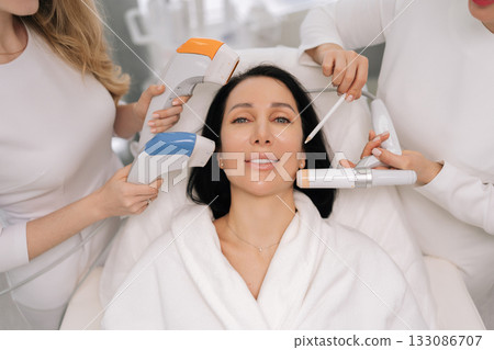 Portrait of middle-aged woman receiving various professional aesthetic treatments including ultrasound and other advanced devices by cosmetologists for skin care and rejuvenation in beauty clinic. Portrait of middle-aged woman receiving various professional aesthetic treatments including ultrasound and other advanced devices by cosmetologists for skin care and rejuvenation in beauty clinic. 133086707