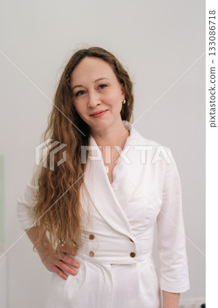 Woman medical professional in stylish white uniform stands confidently indoors against white background, conveying expertise and modern clinic or hospital professionalism. Concept of healthy lifestyle 133086718