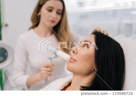 Close-up of female receiving focused ultrasound facial lifting procedure for skin tightening, promoting anti-aging and rejuvenation in professional cosmetology clinic. Concept of facial anti-aging. Close-up of female receiving focused ultrasound facial lifting procedure for skin tightening, promoting anti-aging and rejuvenation in professional cosmetology clinic. Concept of facial anti-aging. 133086728