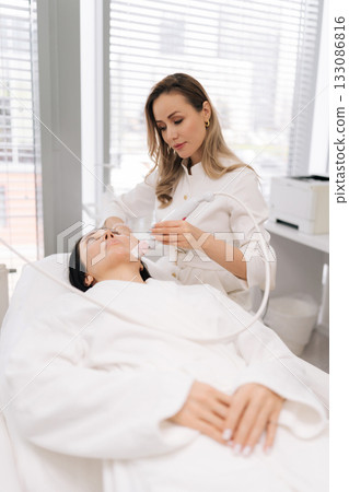 Cosmetologist performing mesotherapy microneedling treatment on middle-aged woman face, applying advanced skincare technology for professional beauty and anti-aging procedures in beauty clinic. Cosmetologist performing mesotherapy microneedling treatment on middle-aged woman face, applying advanced skincare technology for professional beauty and anti-aging procedures in beauty clinic. 133086816