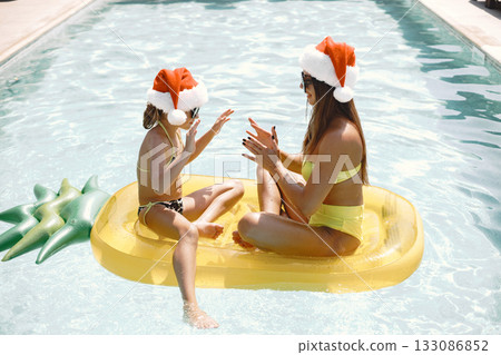 Mother and daughter on inflatable mattress in swimming pool. Celebrating Christmas.Family vacation. Mother and daughter on inflatable mattress in swimming pool. Celebrating Christmas.Family vacation. 133086852