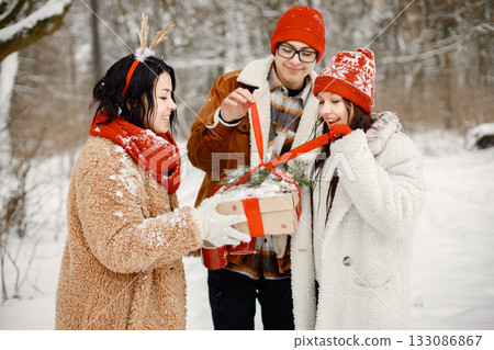 Joyful teens and their beautiful mother spending time together in the winter park. Family holding a gift box. Family wearing warm jackets and knitted hats. Joyful teens and their beautiful mother spending time together in the winter park. Family holding a gift box. Family wearing warm jackets and knitted hats. 133086867