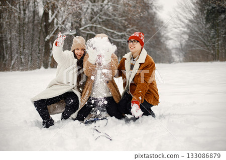 Joyful teens and their beautiful mother spending time together in the winter park. Family riding on a sled. Family wearing warm jackets and knitted hats. Joyful teens and their beautiful mother spending time together in the winter park. Family riding on a sled. Family wearing warm jackets and knitted hats. 133086879