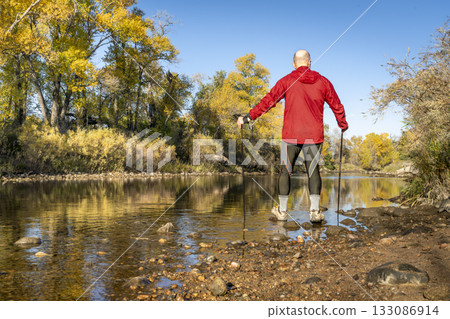 senior male hiker with trekking poles on a shore of the Poudre River in Fort Collins, Colorado, in a fall scenery 133086914