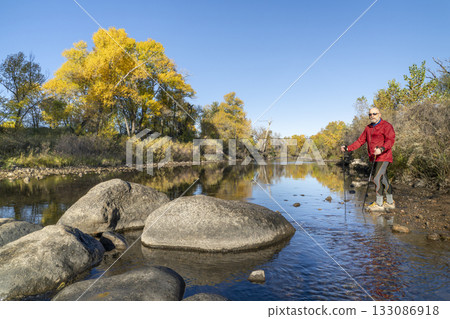 senior make hiker in his 70s with trekking poles on a shore of the Poudre River in Fort Collins, Colorado, fall scenery 133086918