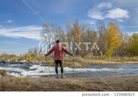 senior make hiker in his 70s with trekking poles on a shore of the Poudre River in Fort Collins, Colorado, fall scenery senior make hiker in his 70s with trekking poles on a shore of the Poudre River in Fort Collins, Colorado, fall scenery 133086923