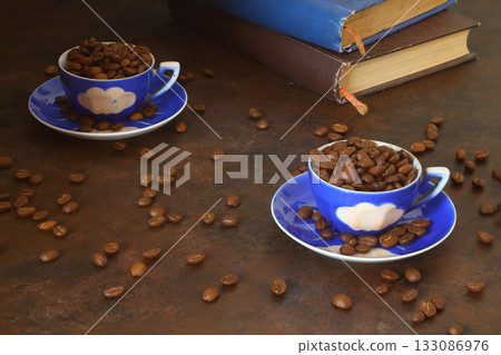 Coffee bean in the blue cups and vintage book stacking on wooden table in morning light 133086976