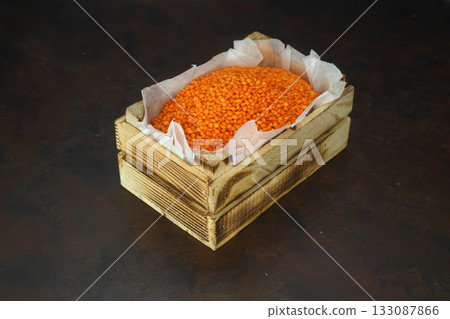 Red Lentil in a small wooden crate, isolated on dark background. With Wooden Spoon. 133087866