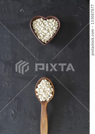 white kidney beans in a heart shaped bowl and wooden spoon on black background.Top view. 133087877