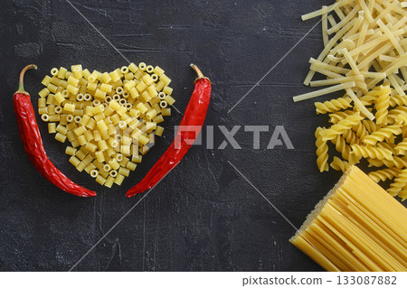 Pasta in the shape of a heart on a black background. With red hot chili peppers. 133087882