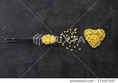 Raw pasta farfalle on wooden spoon on black background. Top view of Italian cuisine ingredient. Raw pasta farfalle on wooden spoon on black background. Top view of Italian cuisine ingredient. 133087887