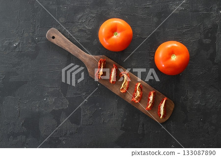 Red sun dried tomatoes with sunlight on black background. Tasty small slices tomato with and olive oil. Red sun dried tomatoes with sunlight on black background. Tasty small slices tomato with and olive oil. 133087890