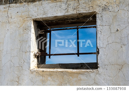 Rustic window frame revealing blue sky through its barred aperture Rustic window frame revealing blue sky through its barred aperture 133087938