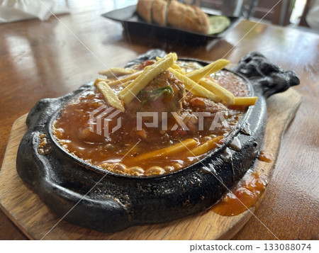 Sizzling Vietnamese Bo Ne with beef, a fried egg, and fries on a hot cast iron platter 133088074