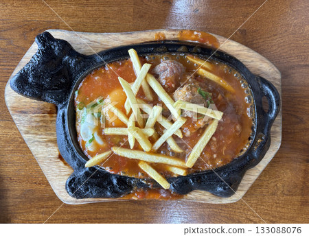 Sizzling Vietnamese Bo Ne with beef, a fried egg, and fries on a hot cast iron platter 133088076