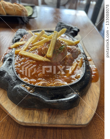 Sizzling Vietnamese Bo Ne with beef, a fried egg, and fries on a hot cast iron platter 133088078