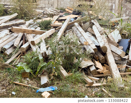 Pile of old wooden beams among grass and weeds. Construction debris, recycling, and raw material texture in outdoor setting. 133088422