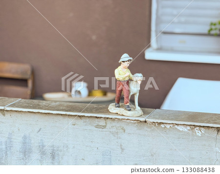 Figurine of boy with dog on wall ledge. Childhood, nostalgia, and gentle emotion through vintage decorative sculpture. 133088438