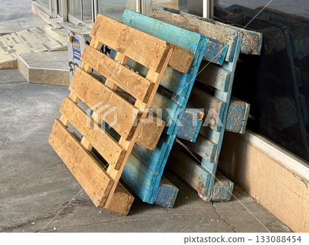Wooden pallets stacked near storefront wall. Construction, recycling, and material reuse concept in urban industrial setting. Wooden pallets stacked near storefront wall. Construction, recycling, and material reuse concept in urban industrial setting. 133088454