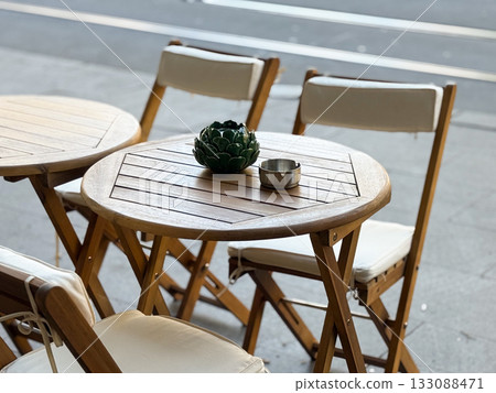 Wooden cafe table with ceramic plant decor and ashtray. Minimal design, sunlight reflection, and serene outdoor dining moment. Wooden cafe table with ceramic plant decor and ashtray. Minimal design, sunlight reflection, and serene outdoor dining moment. 133088471