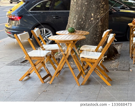 Outdoor wooden table with chairs on city pavement. Urban cafe setting, sunlight, and relaxed atmosphere for social gathering. Outdoor wooden table with chairs on city pavement. Urban cafe setting, sunlight, and relaxed atmosphere for social gathering. 133088473