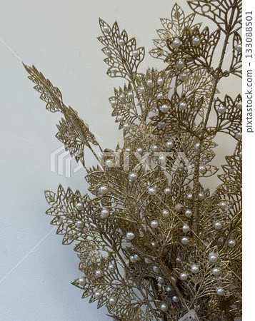 Golden decorative branch with pearl ornaments on wall background. Christmas decoration. Elegant home decor, festive arrangement, and holiday inspiration. 133088501