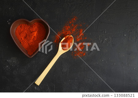 red hot chili peppers powder in heart shaped bowl on black stone table. Love concept. red hot chili peppers powder in heart shaped bowl on black stone table. Love concept. 133088521