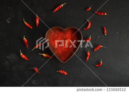 red hot chili peppers powder in heart shaped bowl on black stone table. Love concept. red hot chili peppers powder in heart shaped bowl on black stone table. Love concept. 133088522